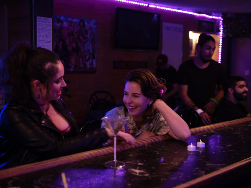 Jamie Hart and Sophie Nation Laughing with Martini Glasses as they sit at the bar on the set of Sloppy Jones. 11 Songs on our Sloppy Playlist this Spring